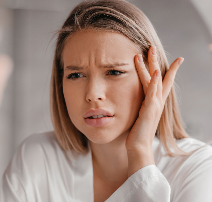 Woman examining forehead in mirror showing signs of dehydration and dry skin.