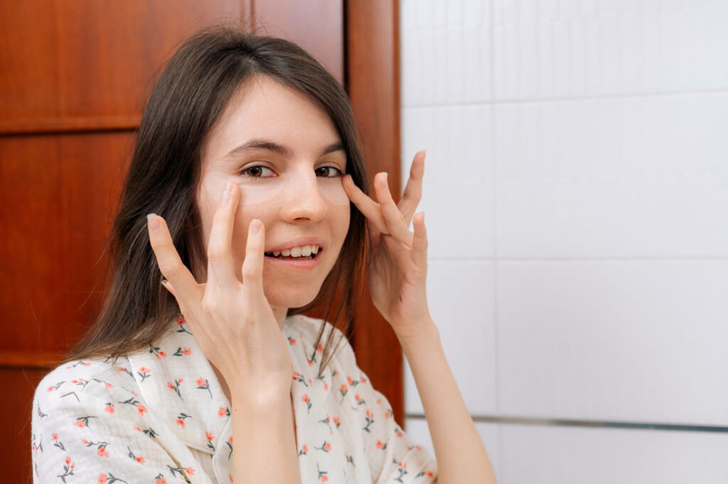 Woman applying under-eye patches to reduce puffiness and lymphatic drainage issues.