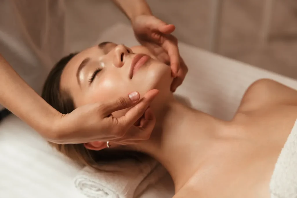 esthetician performing a relaxing facial massage on a woman lying down
