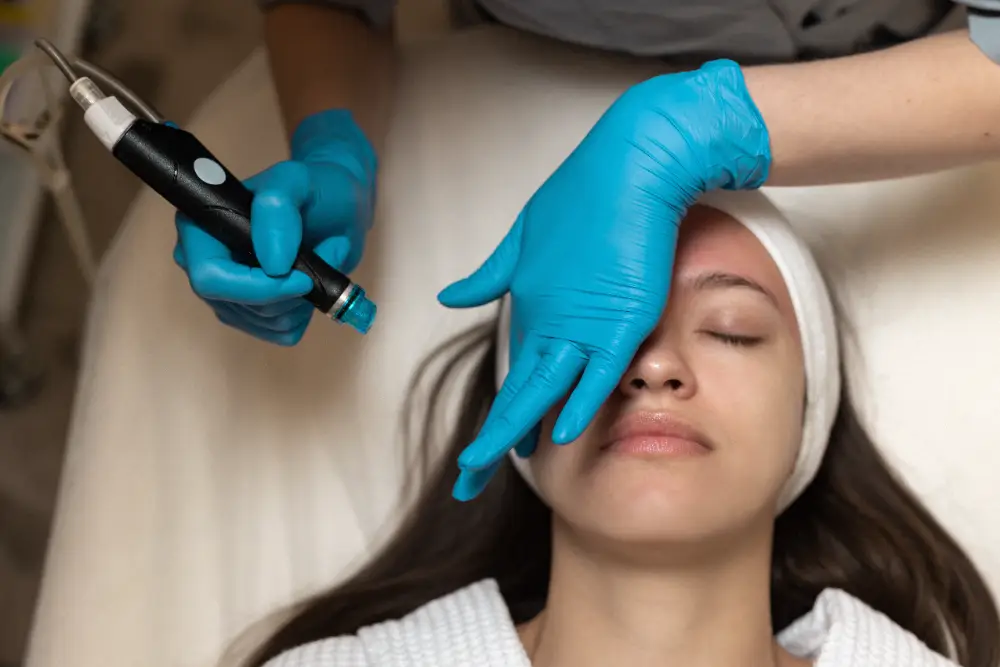 Esthetician performing HydraFacial exfoliation on a woman’s face with a handheld device.