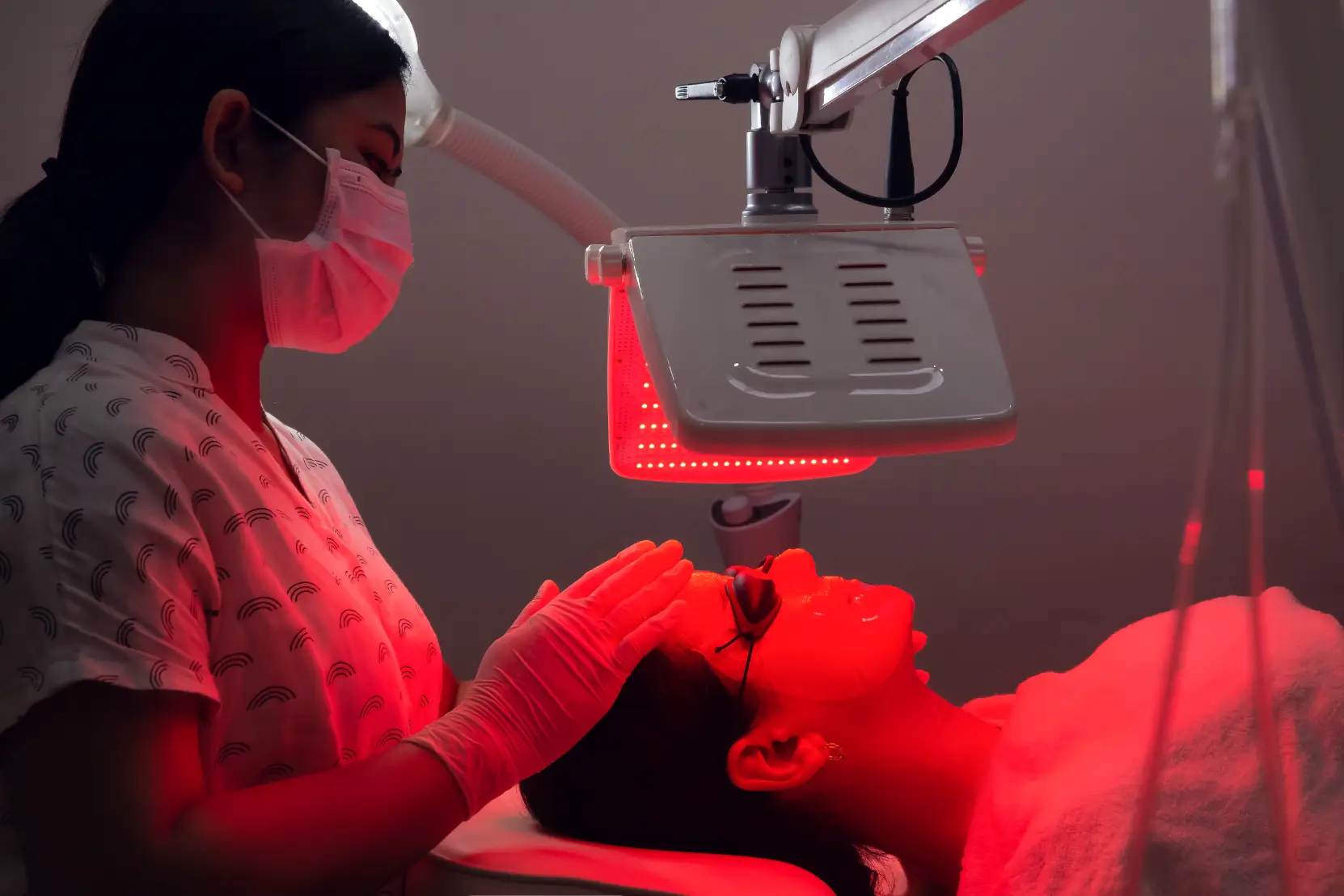 Client receiving LED light facial therapy while wearing protective eye shields during treatment