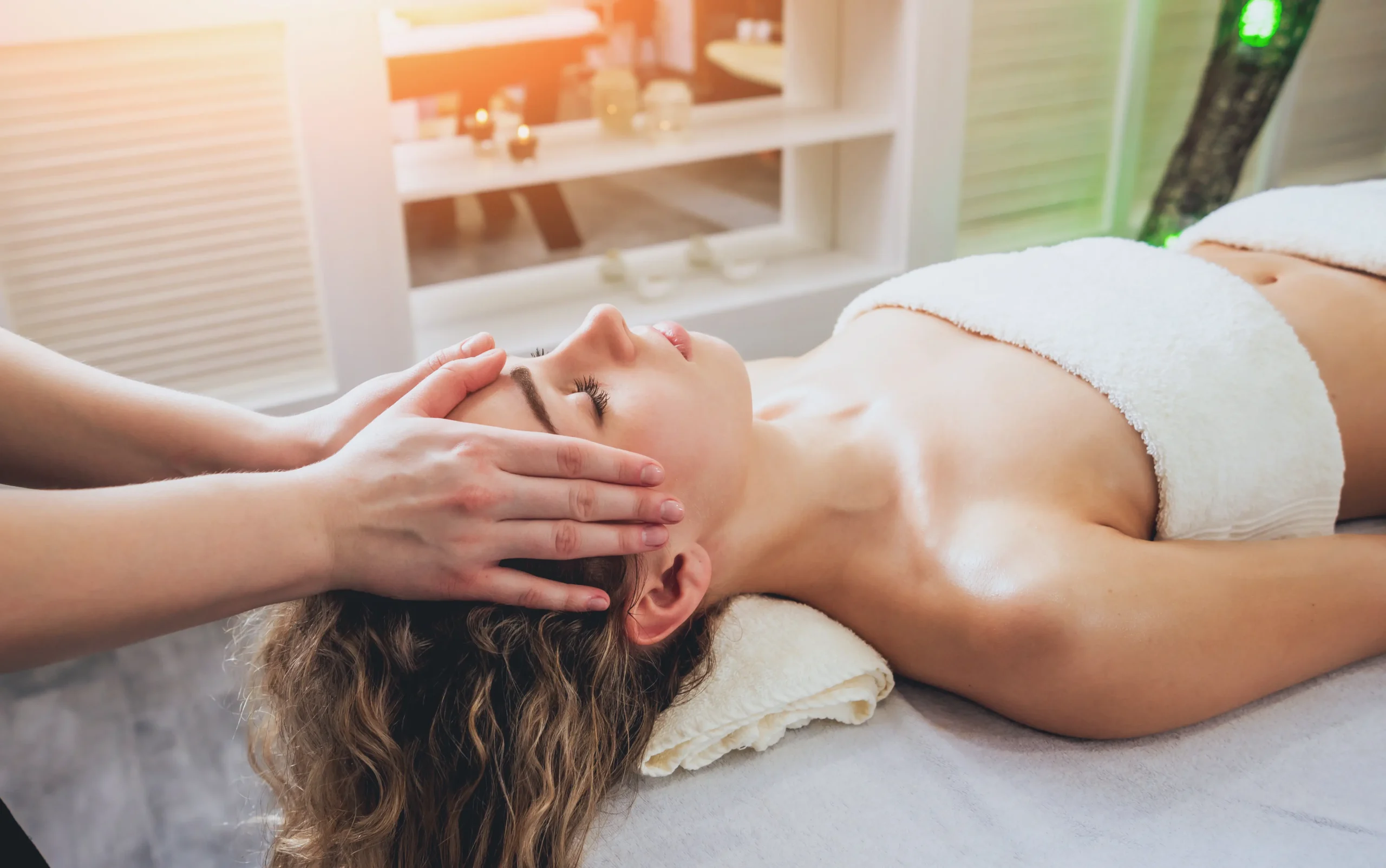 A practitioner wearing gloves applies skincare product to a client lying on a treatment bed in a clinic.